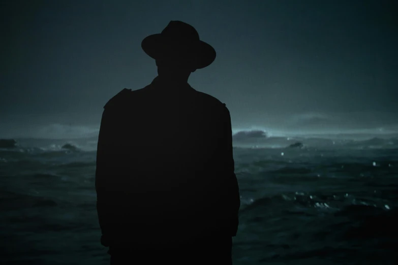 a man standing on top of a beach next to the ocean, an album cover, inspired by roger deakins, pexels contest winner, noir detective and a fedora, night vision, silhouettes of people, mysterious eerie portrait