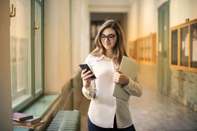 a woman standing in a hallway looking at her cell phone, trending on pexels, renaissance, standing in class, avatar image, holding books, computer