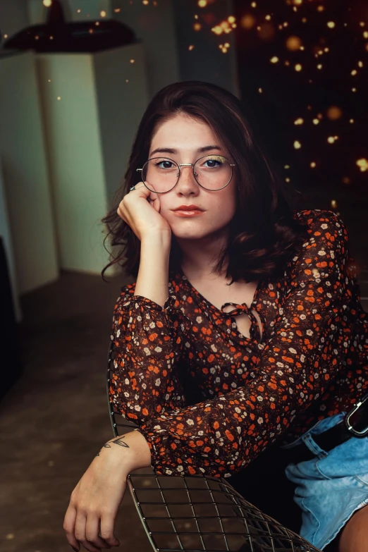 a woman sitting on a chair in a room, a colorized photo, inspired by Elsa Bleda, trending on pexels, photorealism, rounded eyeglasses, handsome girl, rebecca sugar, 18 years old