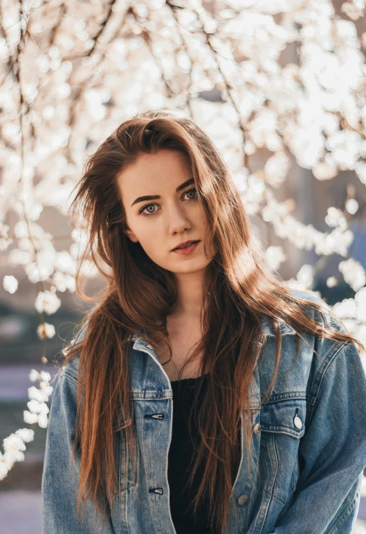 a woman standing in front of a tree with white flowers, inspired by Elsa Bleda, unsplash contest winner, thin long auburn hair, wearing a jeans jackets, perfect face model, lily collins