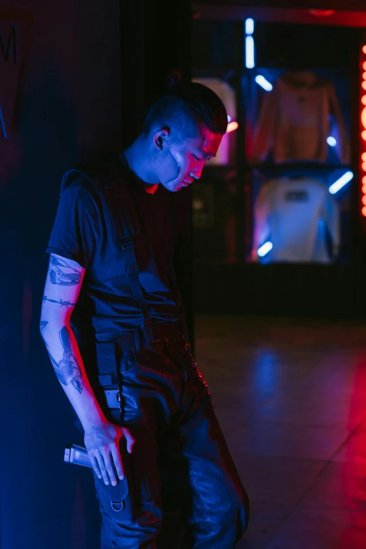 a man leaning against a wall in a dark room, an album cover, inspired by Elsa Bleda, unsplash, visual art, dressed in punk clothing, reflecting light in a nightclub, shaved sides, tactical vests and holsters