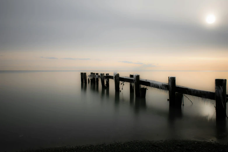 a wooden pier sitting in the middle of a body of water, by Holger Roed, medium format. soft light, long exposure photo, soft light - n 9, grey