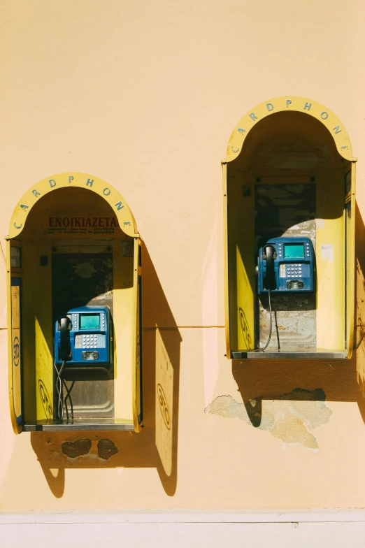 a couple of pay phones sitting on the side of a building, a photo, inspired by Wes Anderson, trending on pexels, art nouveau, yellow walls, naples, sunken, in a sunny day