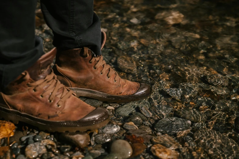 a close up of a person wearing brown shoes, trending on pexels, rugged ranger, standing next to water, copper patina, iconic scene