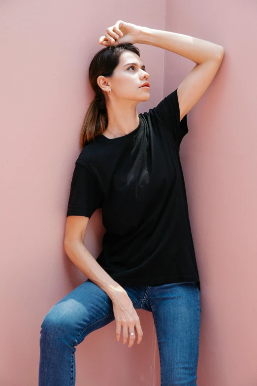 a woman leaning against a pink wall, wearing black tshirt, no - text no - logo, official product image, wide image