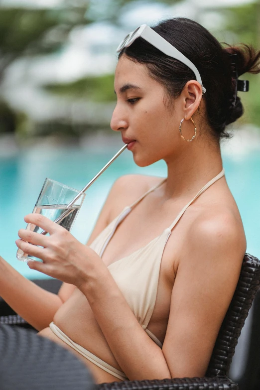 a woman sitting in a chair drinking a glass of water, trending on pexels, wearing two - piece swimsuit, asian features, profile image, with a straw