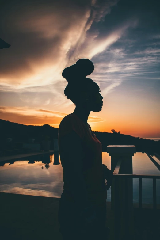 a woman standing in front of a body of water at sunset, shot from roofline, photo of a black woman, portrait featured on unsplash, silhouette of man