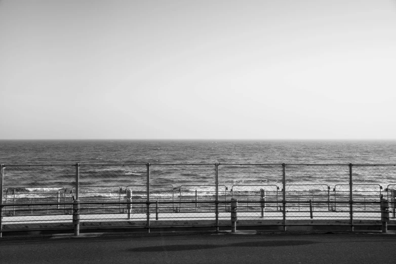 a black and white photo of people looking at the ocean, postminimalism, fences, 8k photo, artwork empty daylight, distant cityscape
