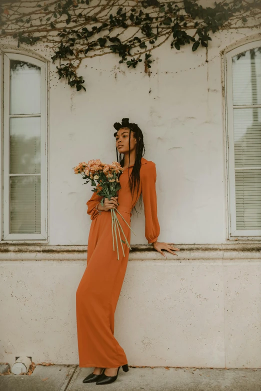 a woman in an orange dress holding a bunch of flowers, pexels contest winner, leaning on the wall, bella poarch, ashteroth, muted brown