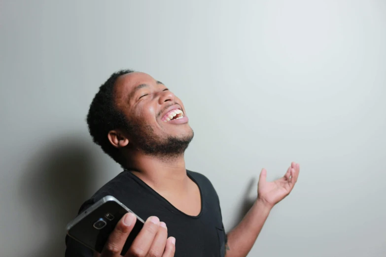 a close up of a person holding a cell phone, an album cover, by Niko Henrichon, pexels, happening, head bent back in laughter, large black smile, hero pose, singing