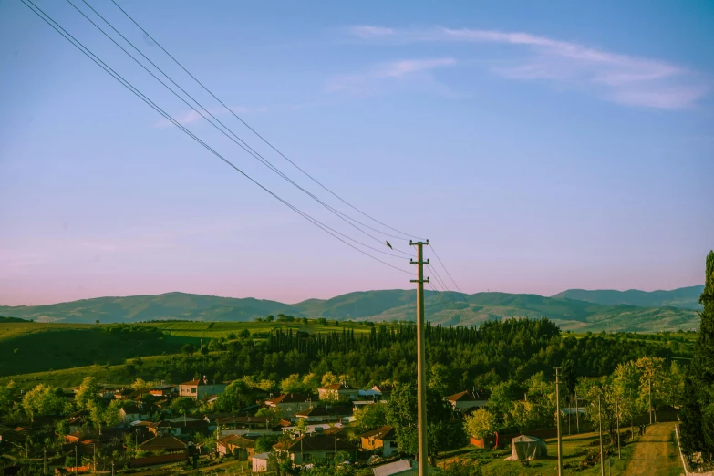 a view of a small town with mountains in the background, inspired by Elsa Bleda, pexels contest winner, telephone wires, ukraine. photography, rolling green hills, summer evening