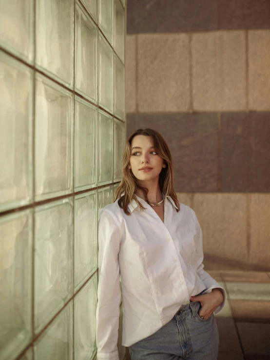 a woman in a white shirt leaning against a wall, by Nina Hamnett, glass ceilings, sydney sweeney, lit up, wearing a linen shirt