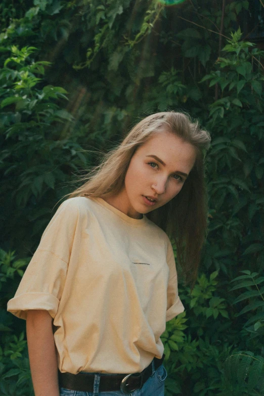 a young woman standing in front of a bush, trending on pexels, realism, wearing a modern yellow tshirt, ukrainian girl, beige hair, 1 9 year old