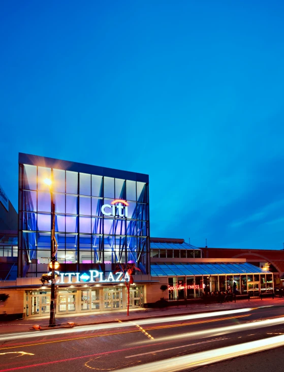 a large glass building sitting on the side of a road, neon lights above shops, capital plaza, profile image, theater