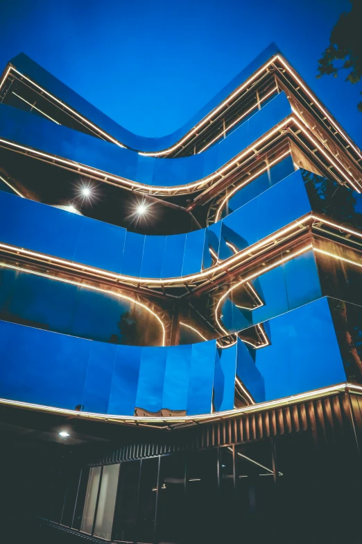 a tall blue building lit up at night, inspired by Zaha Hadid, unsplash contest winner, bauhaus, reflections in copper, curved hallways, detailed and intricate image, golden hour intricate