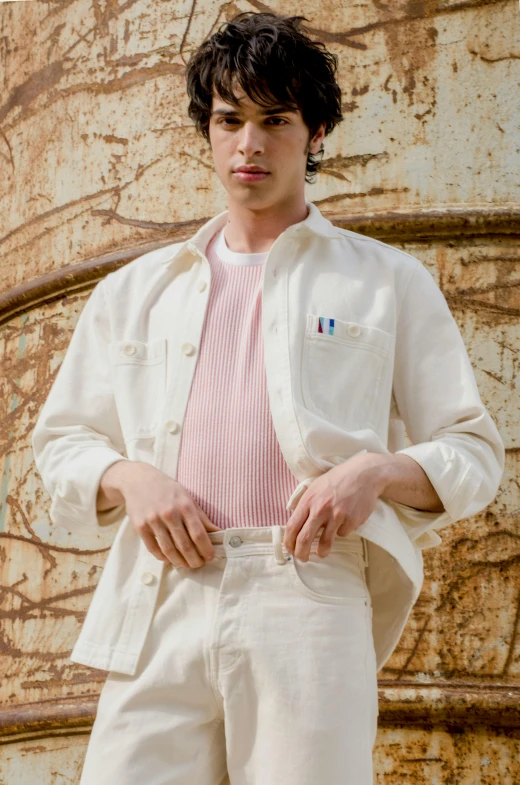 a man standing in front of a rusted building, an album cover, inspired by Louis Hersent, trending on pexels, renaissance, white and light-pink outfit, portrait of timothee chalamet, corduroy, off - white collection