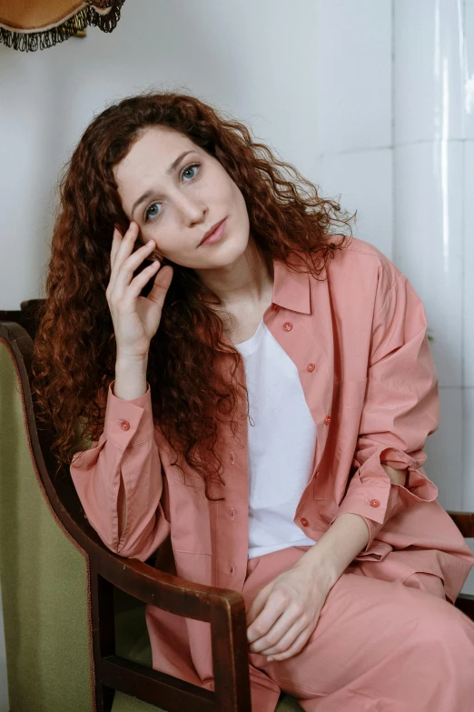 a woman sitting in a chair talking on a cell phone, a portrait, inspired by Anita Malfatti, trending on pexels, renaissance, coral brown hair, curly pink hair, cropped shirt with jacket, wearing white pajamas