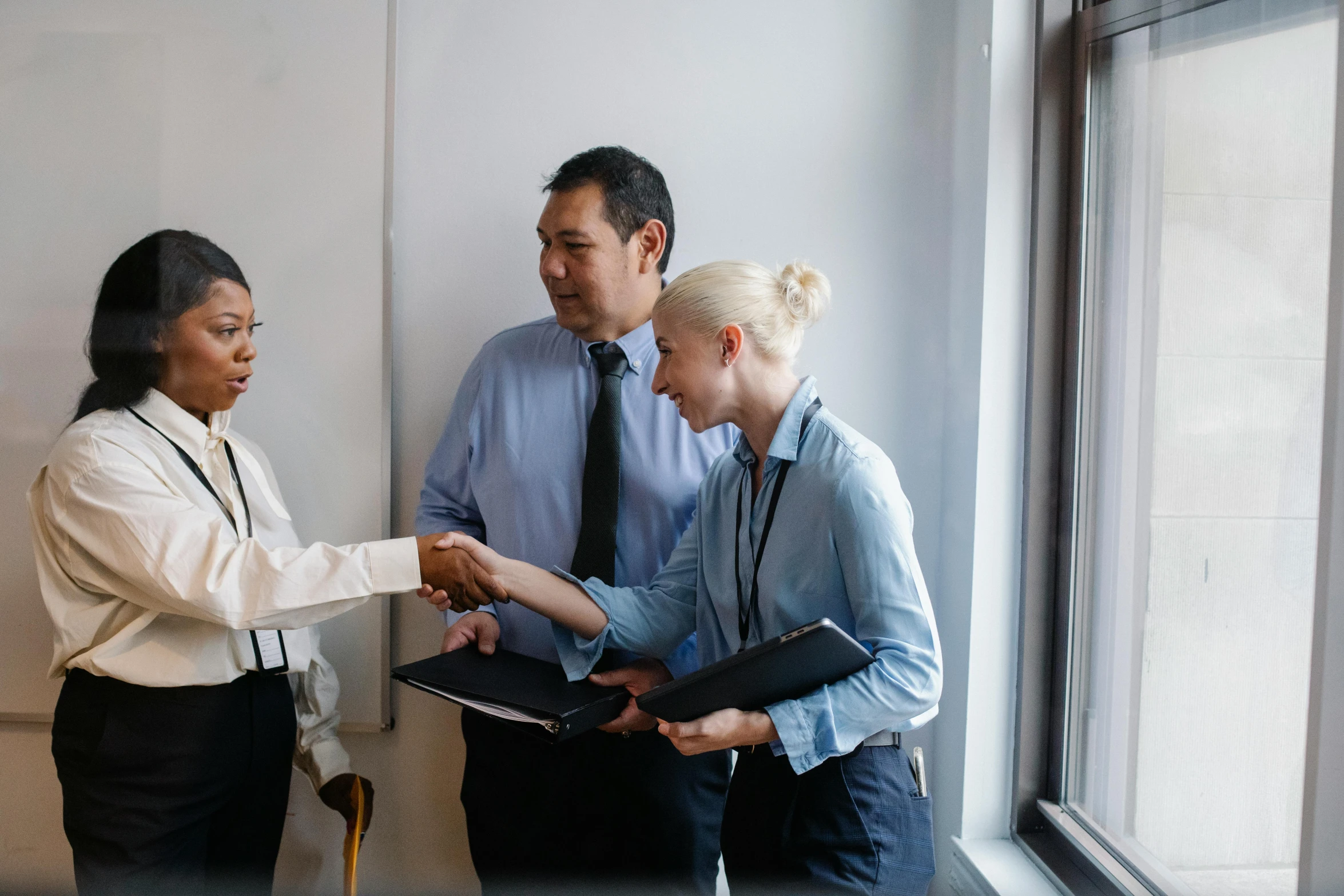 a group of people standing in front of a window, shaking hands, varying ethnicities, lachlan bailey, background image