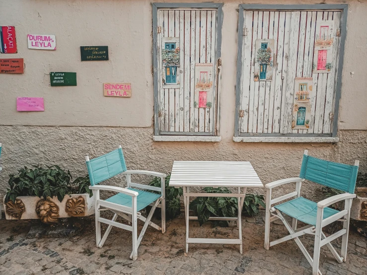 a table and chairs in front of a building, a photo, pexels contest winner, white and teal metallic accents, cottage town, miscellaneous objects, pastelle colors