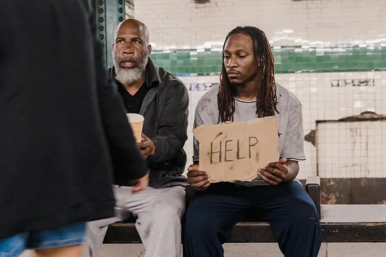 two men sitting on a bench holding a sign, pexels contest winner, homeless, a black man with long curly hair, [ theatrical ], 9/11