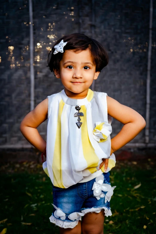 a little girl standing in the grass with her hands on her hips, a portrait, shutterstock contest winner, sleeveless tops, silver and yellow color scheme, ameera al taweel, at a fashion shoot