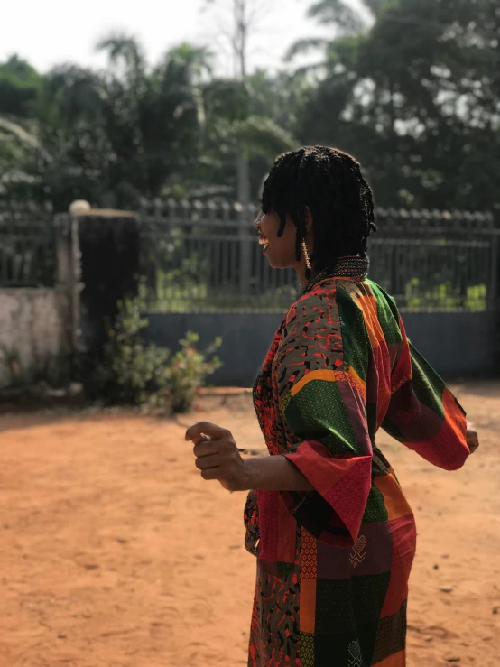 a woman standing on top of a dirt field, an album cover, by Chinwe Chukwuogo-Roy, walking through a suburb, wearing rainbow kimono, profile image, facing away from the camera