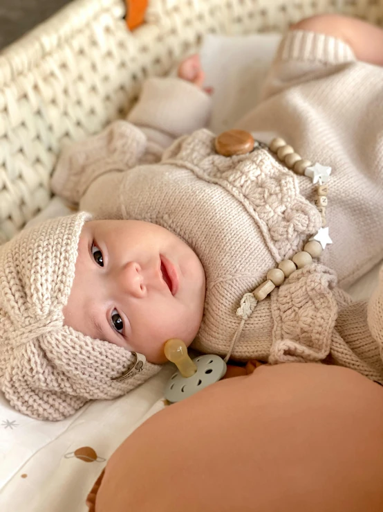 a baby in a knitted outfit laying in a crib, instagram, natural wood top, official product photo, beige, close up face detail