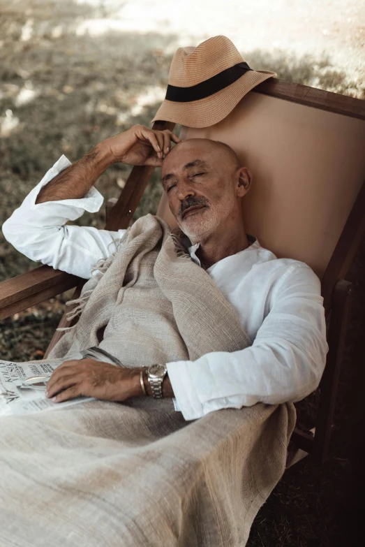 a man sitting in a chair with a hat on, inspired by Edi Rama, trending on unsplash, renaissance, wearing white pajamas, sri lanka, wearing a linen shirt, conde nast traveler photo