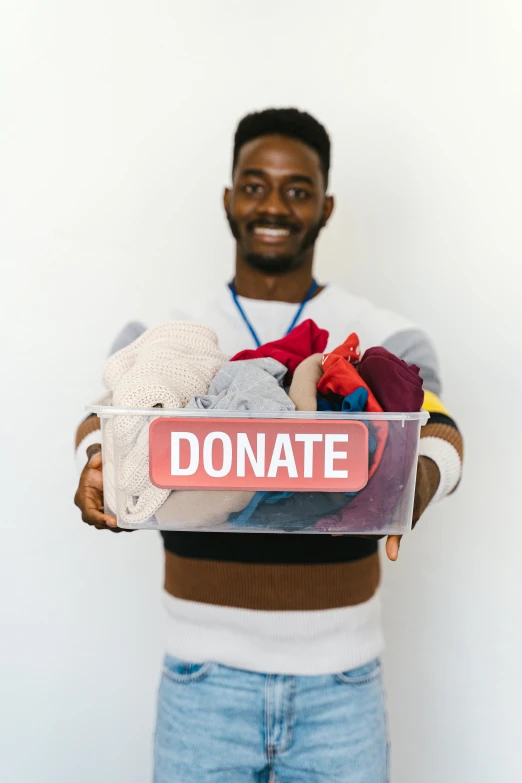 a man holding a sign that says donate, a colorized photo, pexels contest winner, clothes fully on, essence, mittens, college