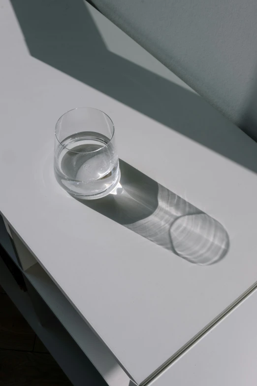 a glass of water sitting on top of a table, 3 - d shadows, on a white table, ignant, water line surface