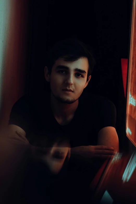 a man sitting at a table in a dark room, a character portrait, pexels contest winner, photorealism, 18 years old, against a red curtain, azimov, desaturated