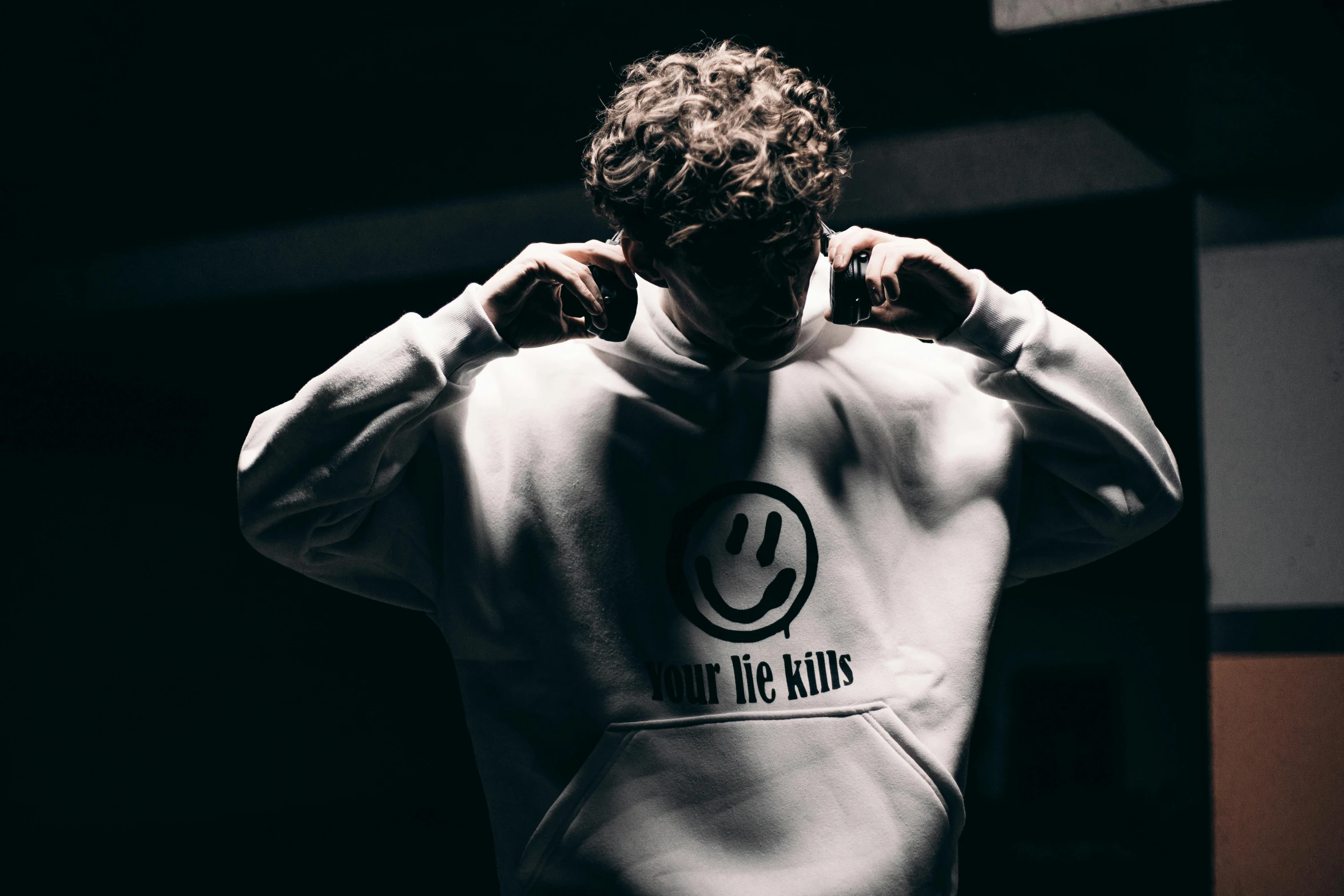 a man standing in a dark room with his hands on his head, an album cover, trending on pexels, graffiti, white sweater, smiley, hoodie, thumbnail