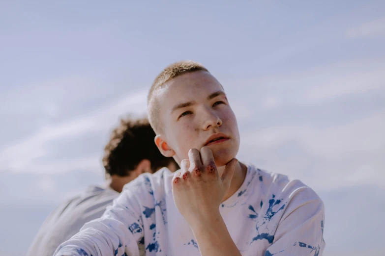 a young boy standing on top of a sandy beach, an album cover, trending on pexels, realism, white freckles, two young men, hand on her chin, albino white pale skin