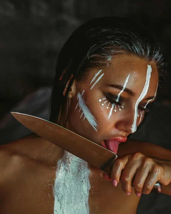 a woman with white paint on her face holding a knife, a cave painting, inspired by Elsa Bleda, trending on pexels, photoshoot for skincare brand, wielding kunai, slightly erotic, ready to eat