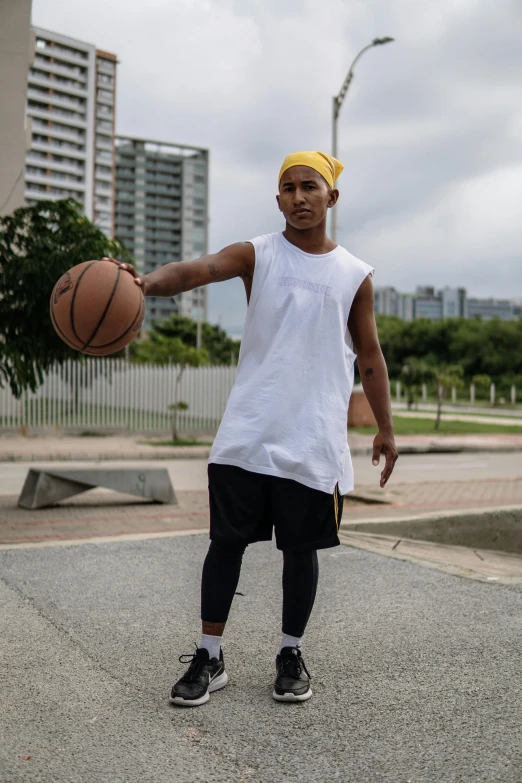 a man standing on a basketball court holding a basketball, dribble, in sao paulo, street clothing, wearing : tanktop, baggy