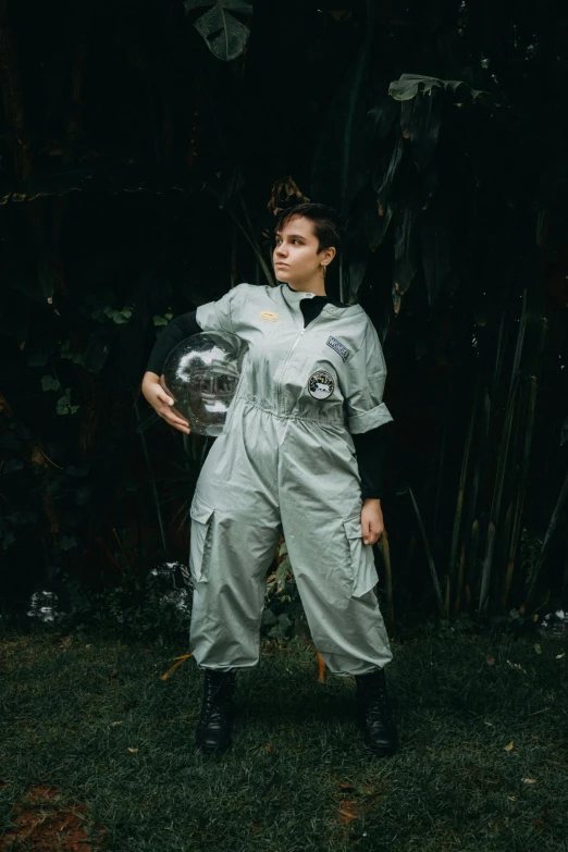 a woman standing on top of a lush green field, an album cover, inspired by Elsa Bleda, pexels contest winner, wearing human air force jumpsuit, in a space cadet outfit, on a gray background, portrait of mad lady scientist