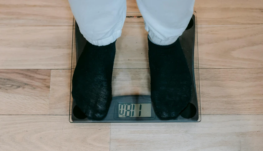 a person standing on a scale on a wooden floor, by Adam Marczyński, pexels, wearing jeans and a black hoodie, 🦩🪐🐞👩🏻🦳, surgery, flat color