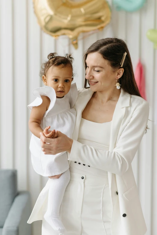 a woman holding a baby in her arms, wearing white dress, diverse outfits, wearing a white button up shirt, wearing white suit