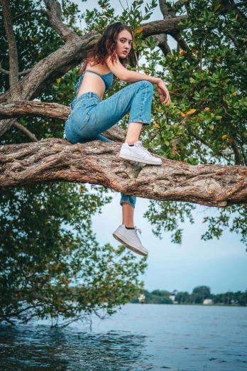 a woman sitting on top of a tree branch, trending on pexels, wearing jeans, non binary model, wearing white sneakers, very accurate photo