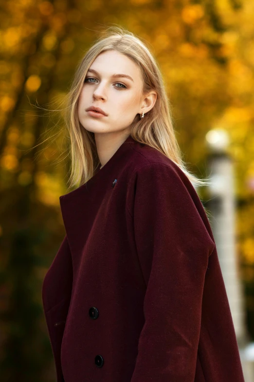 a woman in a maroon coat posing for a picture, trending on pexels, sleek blond hair, looking off to the side, dolman, autum