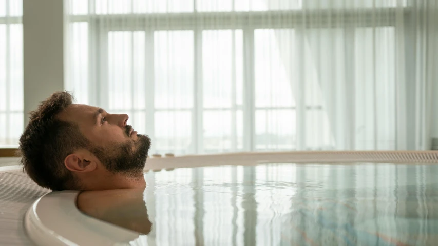 a man laying in a bathtub next to a window, wellness pool, over water, out of body experience, indoor pool
