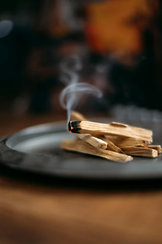 a black plate sitting on top of a wooden table, sage smoke, holding a burning wood piece, tiny sticks, close - up photograph