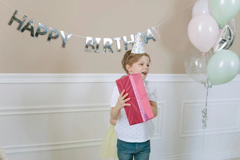 a little girl holding a birthday present in front of balloons, by Alice Mason, pexels, wearing silver silk robe, banner, at the party, avatar image