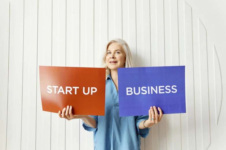 a woman holding up signs that say start up and business, an album cover, pexels, private press, square, biotech, modest, pair of keycards on table
