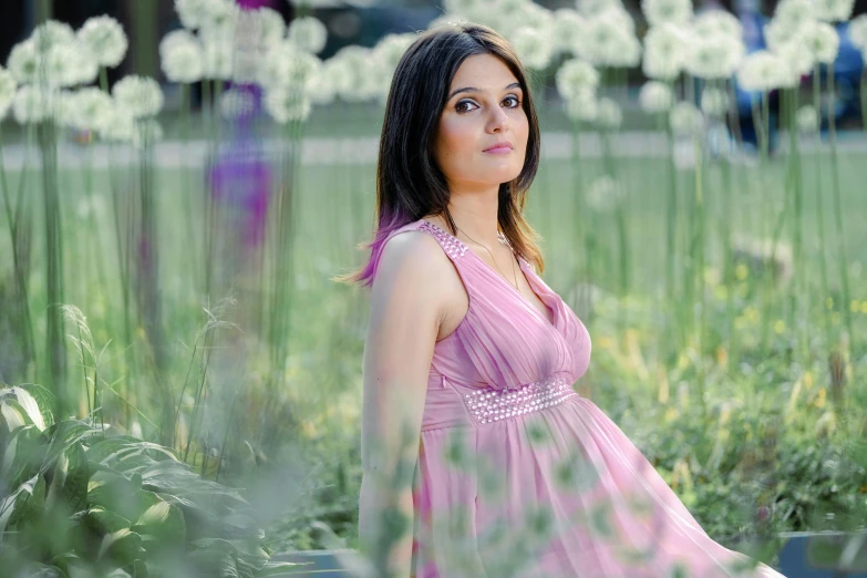 a woman sitting on a bench in a field of flowers, a picture, pregnant, portrait of sherlyn chopra, wearing a pink dress, taken in the late 2010s