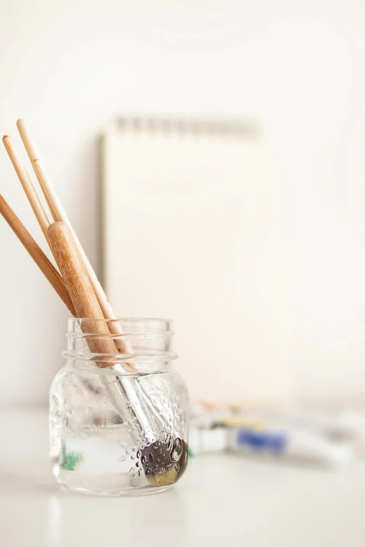 a jar filled with toothbrushes sitting on top of a table, a photorealistic painting, unsplash, visual art, holding paintbrushes, white studio background, chopsticks, morning detail