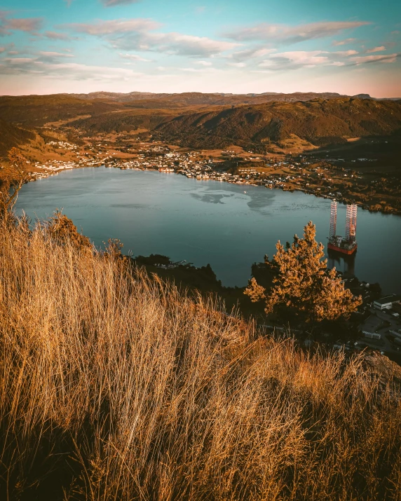 a large body of water sitting on top of a lush green hillside, a picture, by Jesper Knudsen, pexels contest winner, small town surrounding, golden glow, thumbnail, high quality screenshot