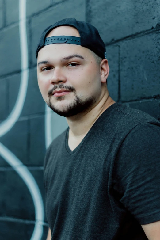 a man standing in front of a wall with graffiti on it, an album cover, inspired by Eddie Mendoza, closeup headshot portrait, thicc, a handsome, rubenesque