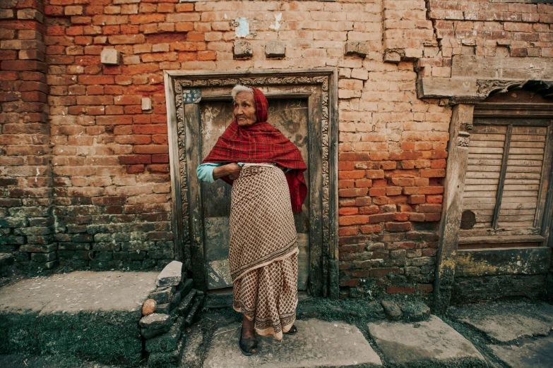 a woman standing in front of a brick building, inspired by Steve McCurry, pexels contest winner, nepal, tight wrinkled cloath, about to enter doorframe, patterned clothing