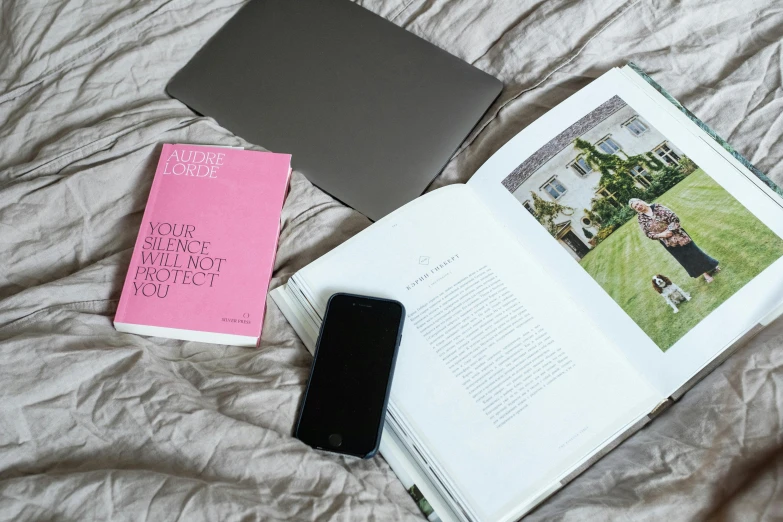 an open book sitting on top of a bed next to a cell phone, a picture, laptops, pink and grey muted colors, thumbnail, homes and gardens